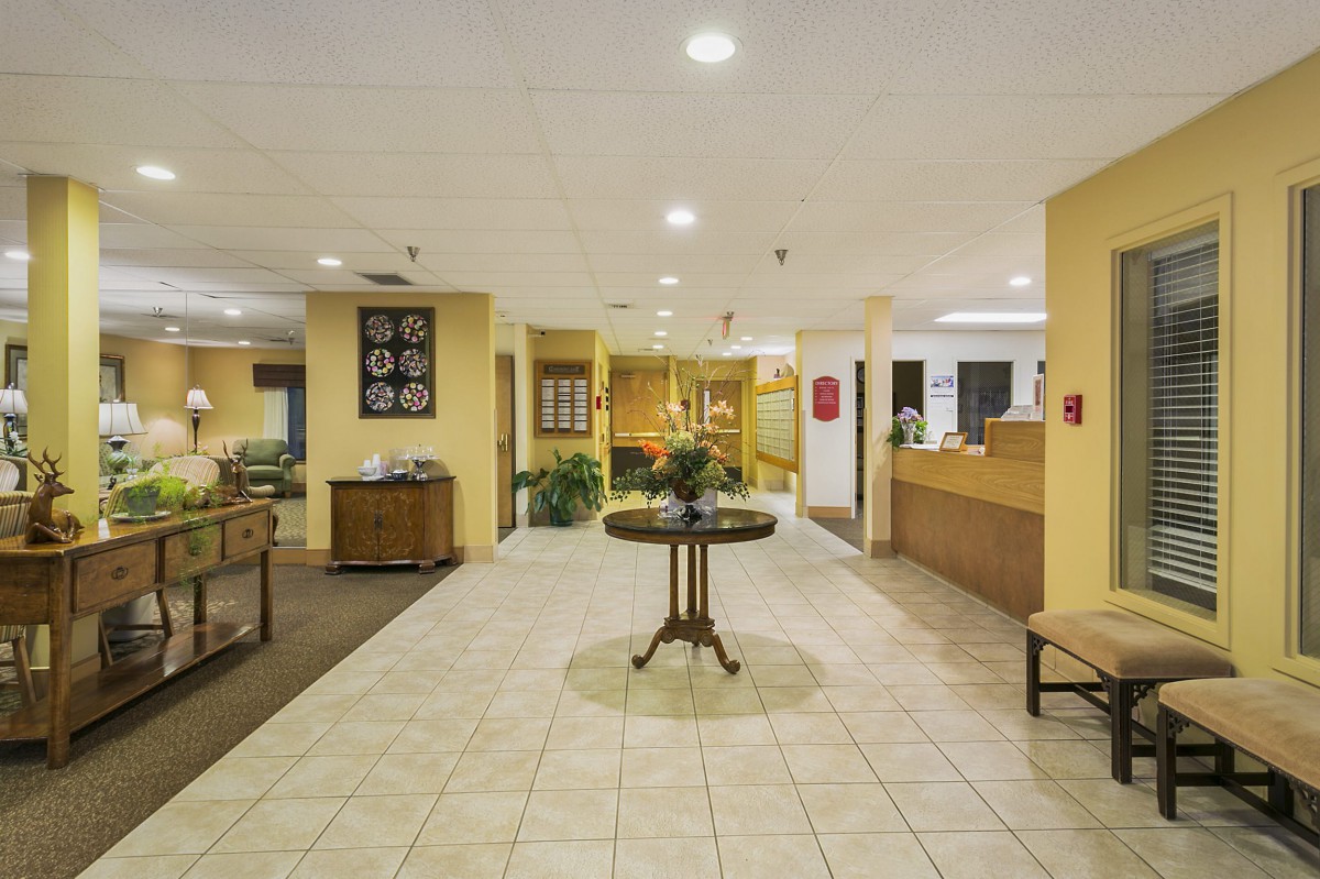 A spacious hotel lobby with a central table displaying a floral arrangement, surrounded by reception desks and seating areas.