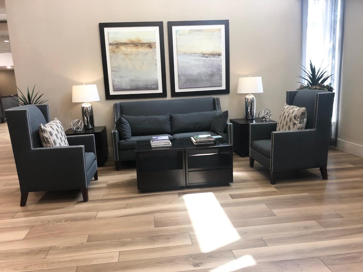 A modern living room featuring a dark sofa and chairs, wooden flooring, complemented by lamps and abstract artwork.