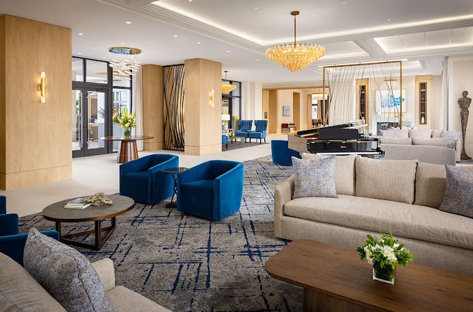 A modern and luxurious hotel lobby featuring comfortable seating with blue chairs and sofas, complemented by a stylish chandelier.