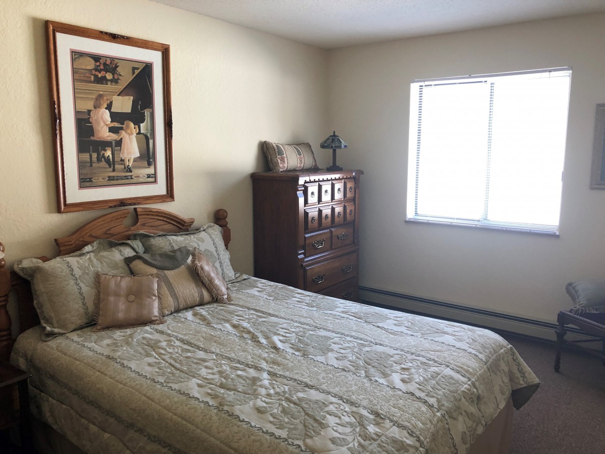A cozy bedroom with a large bed, dresser, and artwork on the wall.
