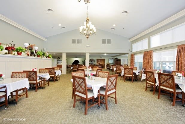 An elegant and spacious dining room with tables and chairs, featuring a central chandelier.