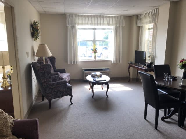 A cozy living room with a sofa, armchair, and coffee table, featuring neutral tones and a window allowing natural light.