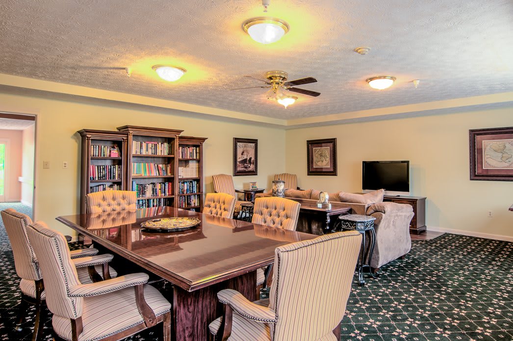 A cozy library room with bookshelves, comfortable seating, and a large table.