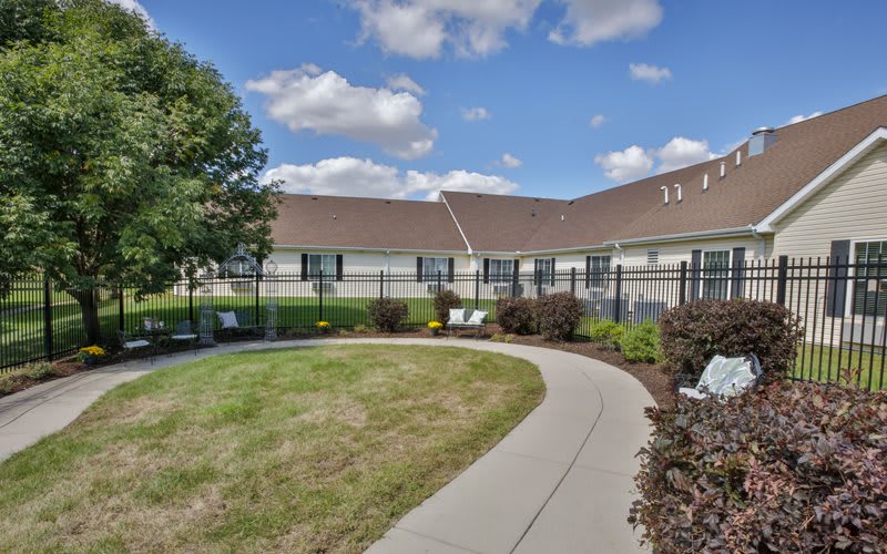 A scenic view of a building with a pathway surrounded by greenery and trees under a partly cloudy sky.