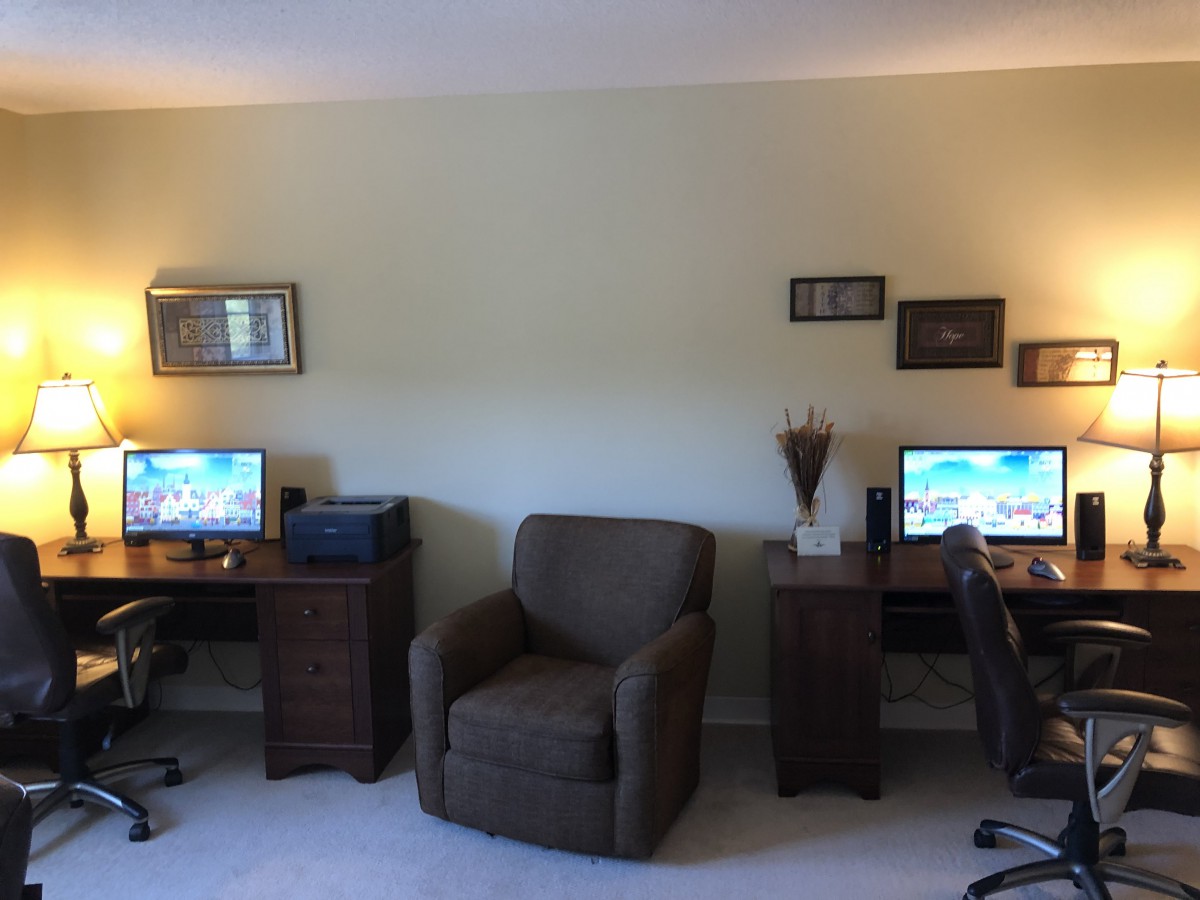 A cozy home office setup with two workstations, featuring computers and comfortable seating.