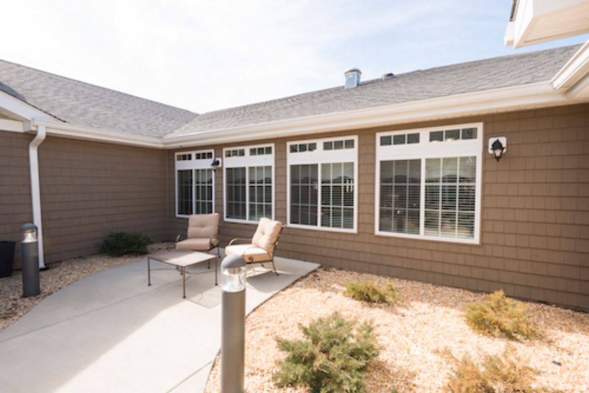 A sunny patio with comfortable chairs and large windows on the house exterior.