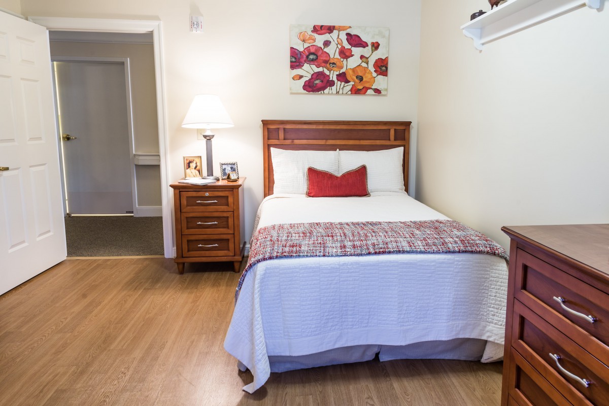 A cozy bedroom with a neatly made bed, nightstand, and warm lighting.