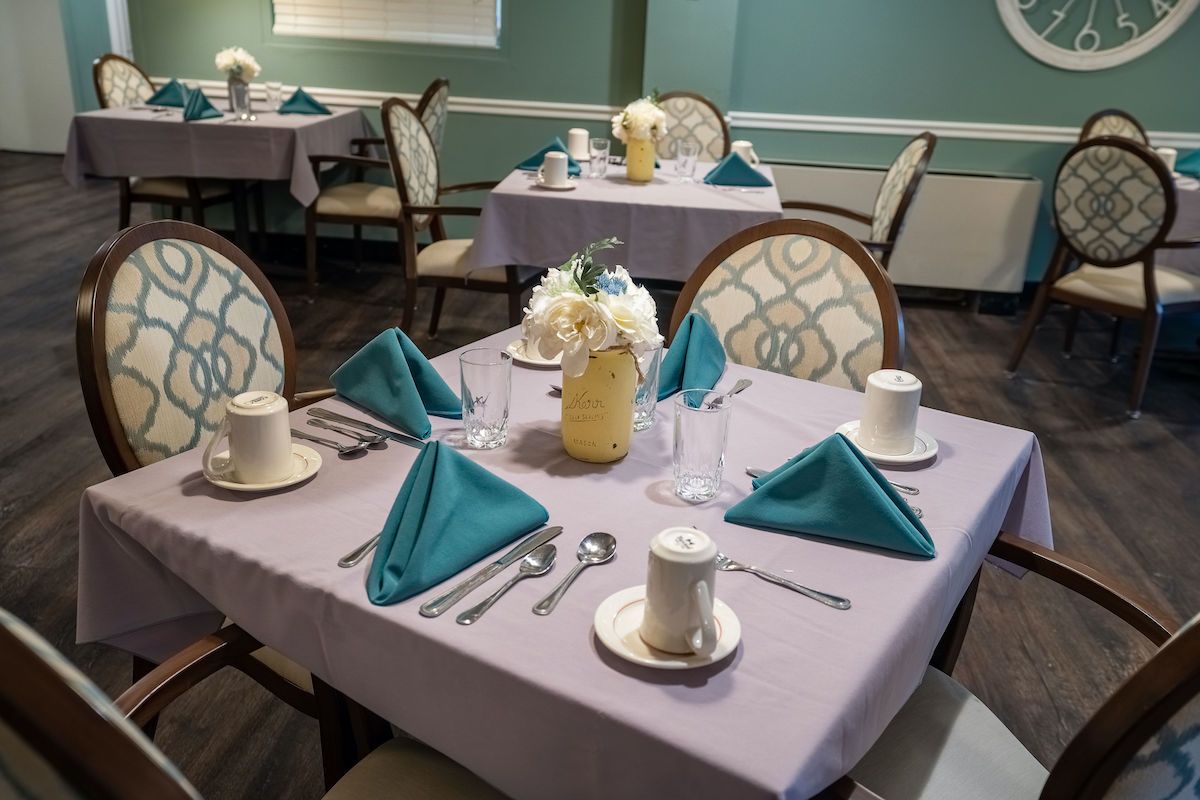 A neatly arranged dining table with teal napkins and floral centerpiece.