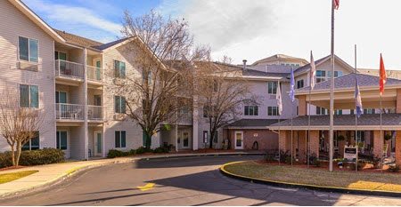 A residential apartment building with a driveway and trees in the foreground.