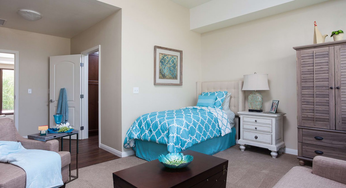 A cozy bedroom featuring a single bed with aqua bedding, a nightstand with a lamp, and decorative wall art.