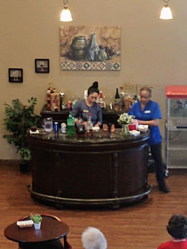 Two people working behind a bar counter in an indoor setting with various beverages and decor.