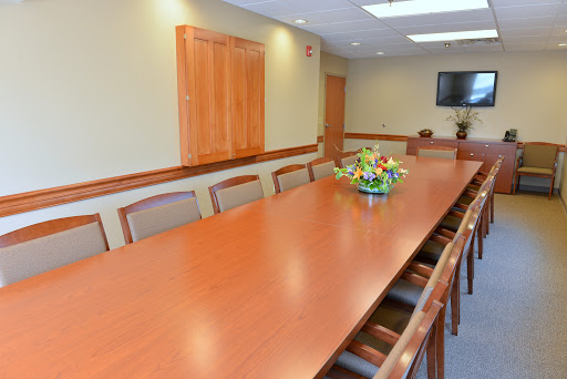 A spacious conference room featuring a long wooden table and a floral centerpiece, designed for meetings.
