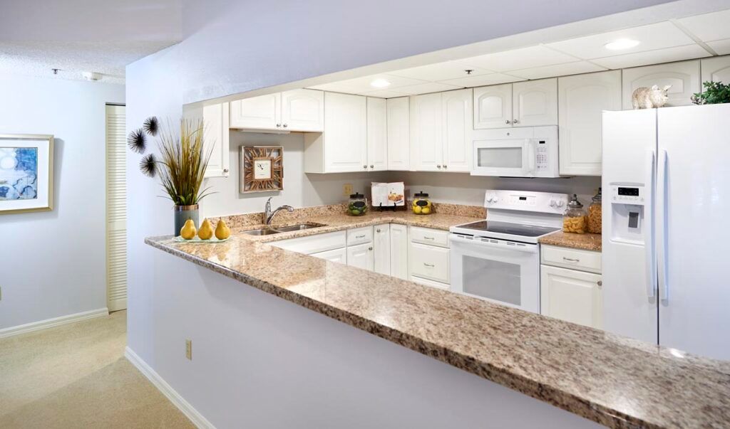A modern kitchen with white cabinets, a granite countertop, and various appliances.