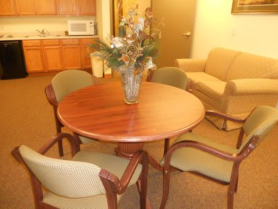 A small meeting room with a round table, four chairs, and a vase centerpiece.