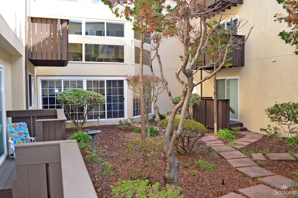 A peaceful courtyard garden surrounded by residential buildings, featuring trees and shrubs.
