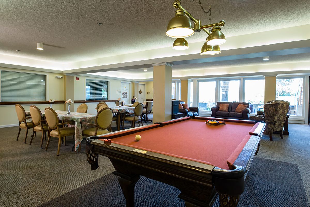 A cozy game room featuring a pool table with a red felt surface, accompanied by comfortable seating and elegant lighting.
