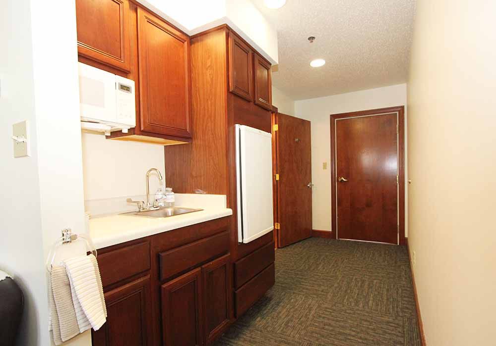 A compact kitchen area featuring wooden cabinets, a microwave, sink, and refrigerator.