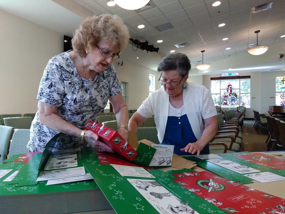 Two senior volunteers wrapping gifts together.