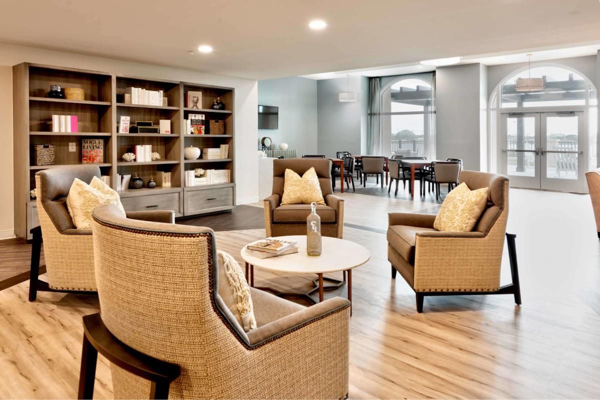 A modern living room with comfortable wicker chairs, a round coffee table, and a large bookshelf under soft lighting.