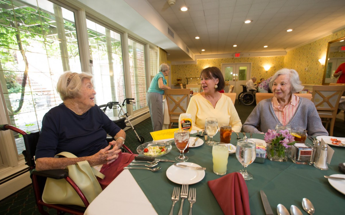A group of elderly people enjoying a meal and conversation at a communal dining table.