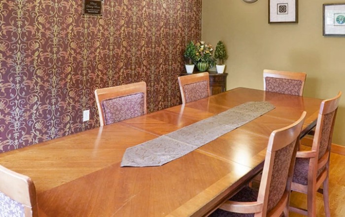 A dining room with a wooden table and chairs, decorated with plants.