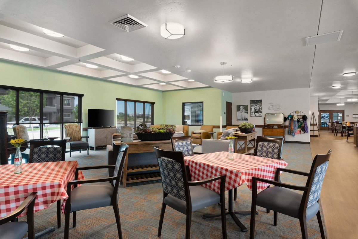 A spacious and well-lit dining area with tables and chairs, featuring a television and large windows.