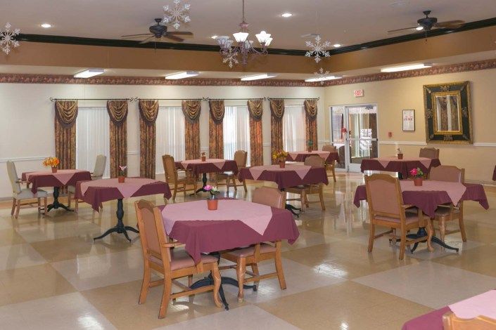A spacious dining area with neatly arranged tables and chairs, featuring decorative curtains and overhead lighting.