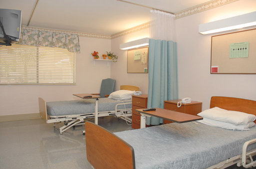 A well-lit and organized hospital patient room featuring two adjustable beds, a privacy curtain, and basic furniture.