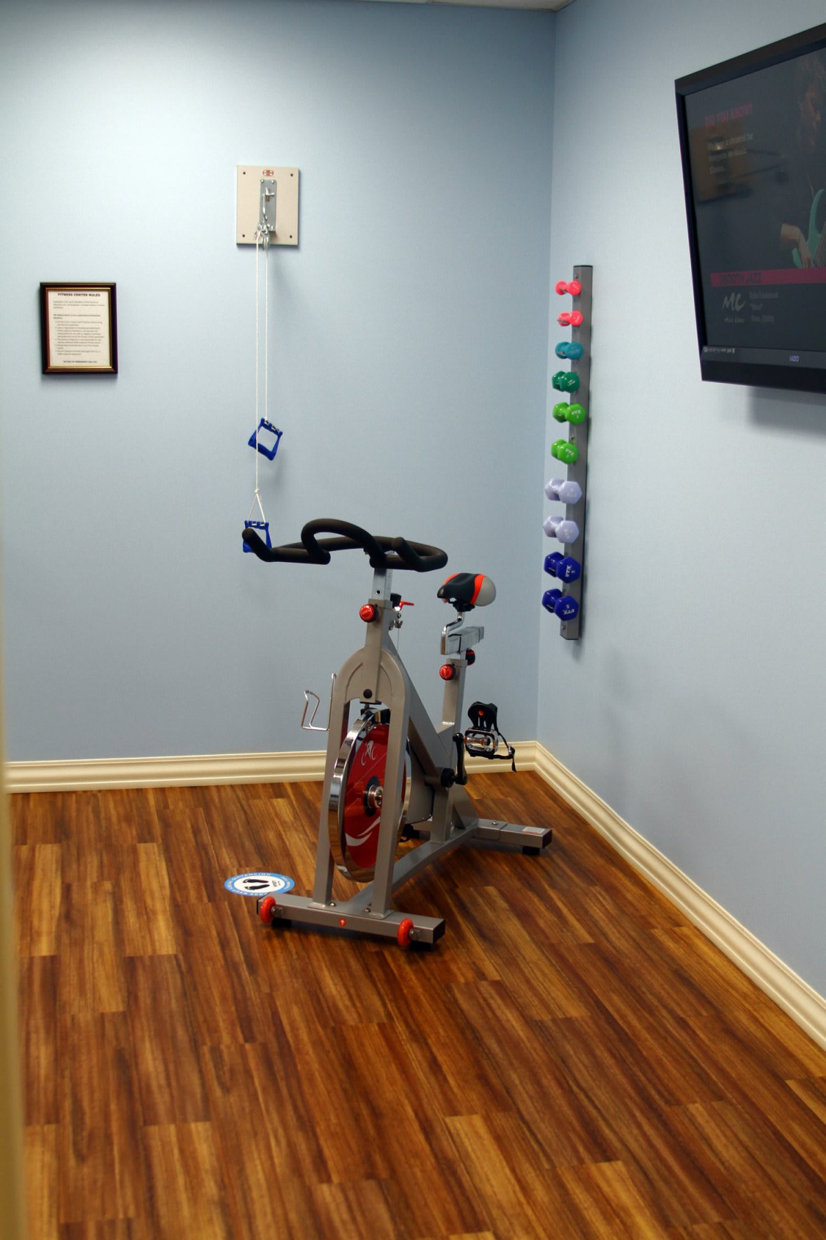 A small home gym setup with a stationary bike and a rack of weights against the wall.