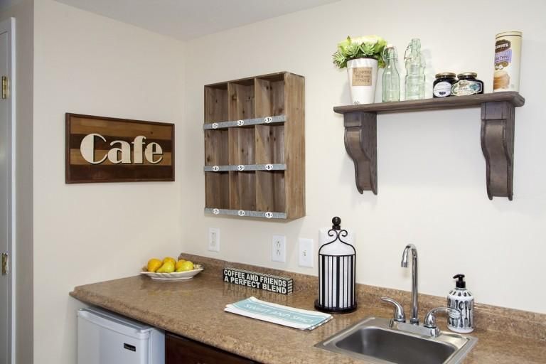 A cozy kitchen corner with rustic shelves, a 'Cafe' sign, and countertop decor.