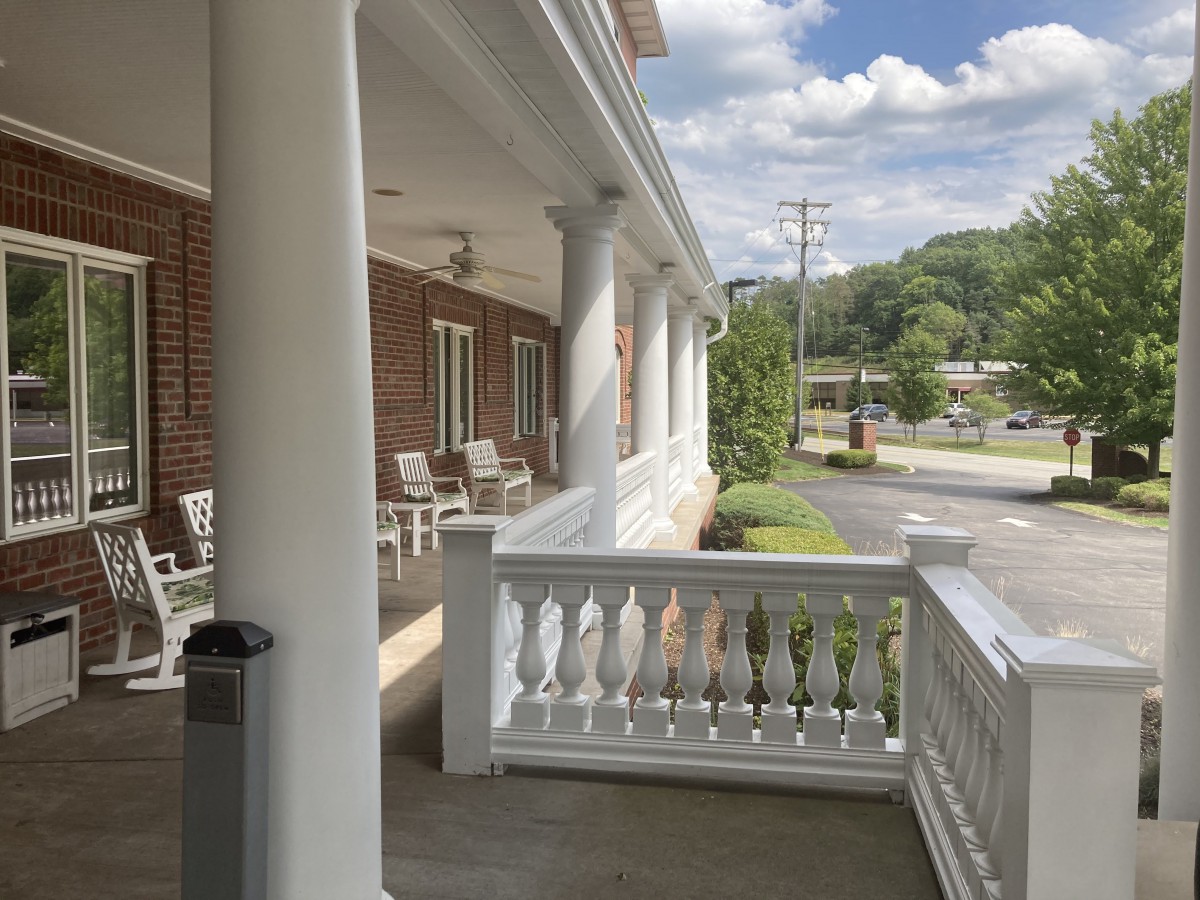 A porch with white columns and chairs overlooking a street.