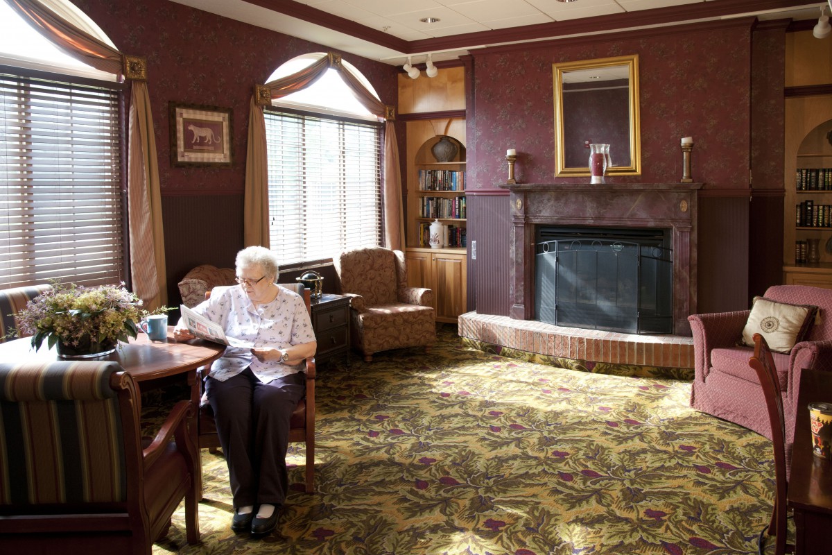 An elderly person reading in a cozy living room with a fireplace.