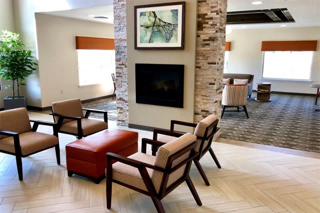 A modern seating area with a fireplace, featuring comfortable chairs and artwork in a well-lit space.
