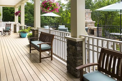 A cozy porch with wooden seating, cushions, and vibrant potted plants.