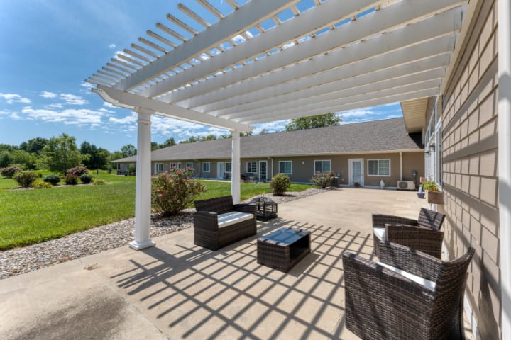 A shaded patio with outdoor furniture under a pergola on a sunny day.