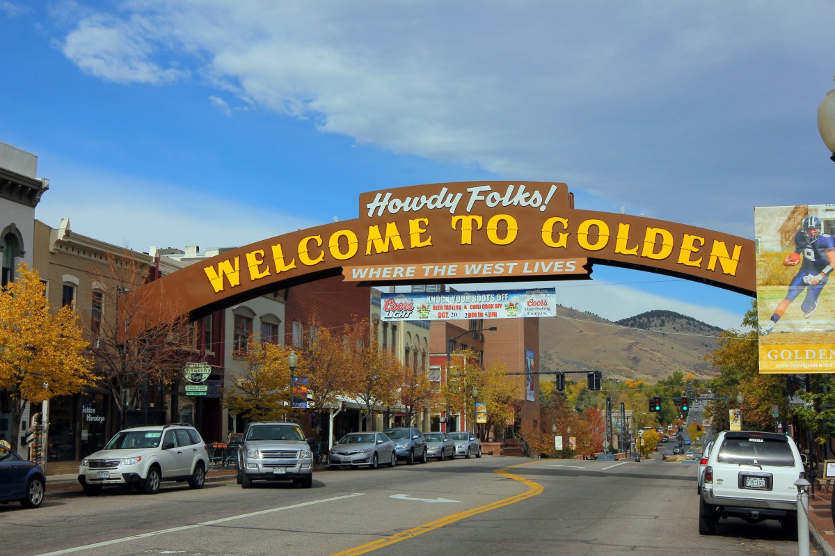 Welcome to Golden sign arching over a street lined with parked cars and buildings.