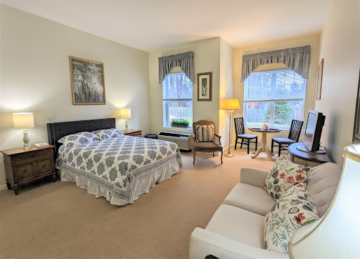A cozy and well-lit bedroom featuring a comfortable bed, seating area, and natural light from the windows.