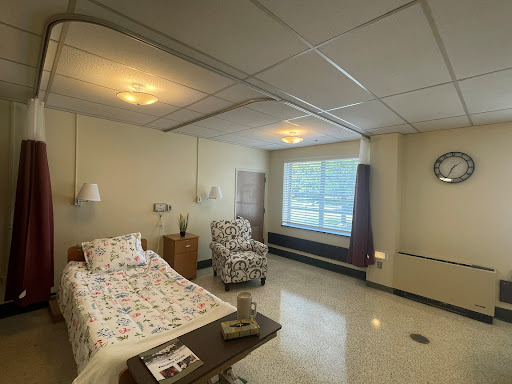 A well-lit and comfortable hospital patient room featuring a bed, armchair, and large window.