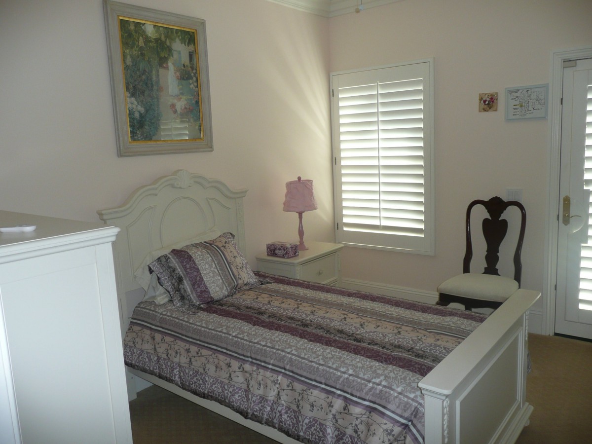 A cozy bedroom with a single bed, lamp, painting, and window shutters.