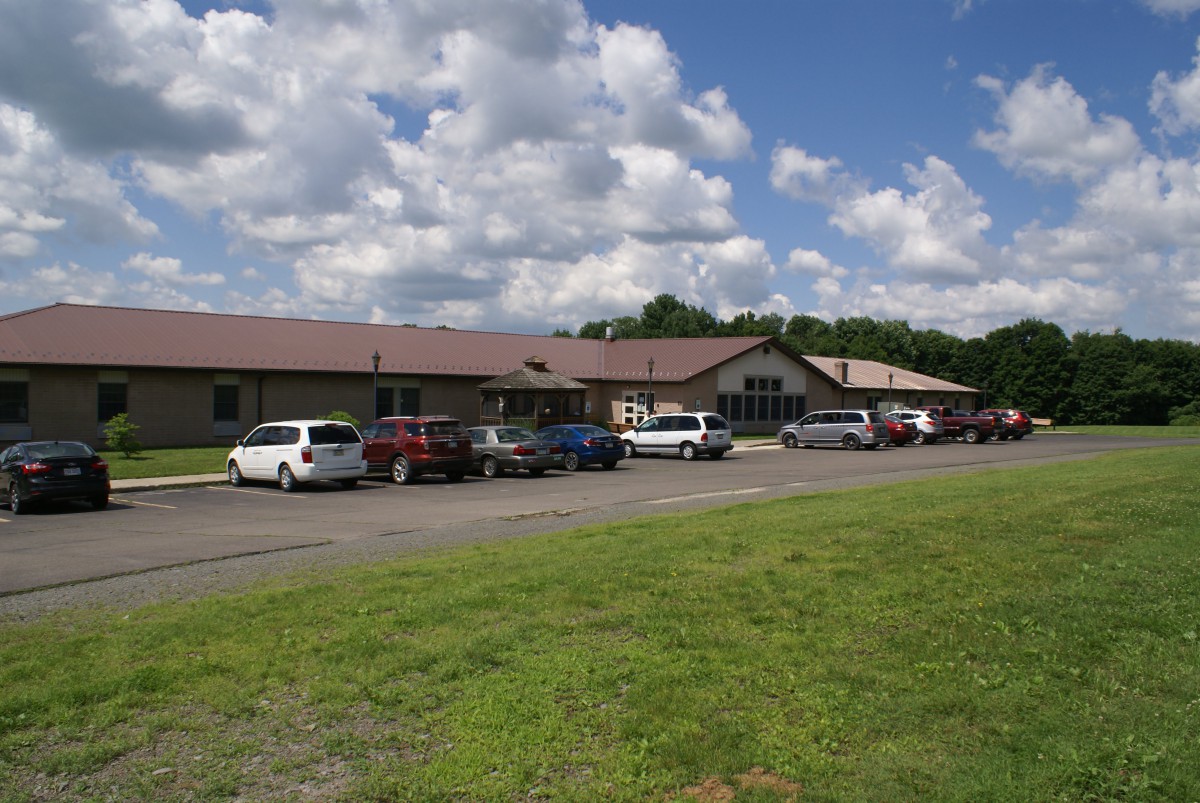 A rural building with a parking lot and several cars under a partly cloudy sky.