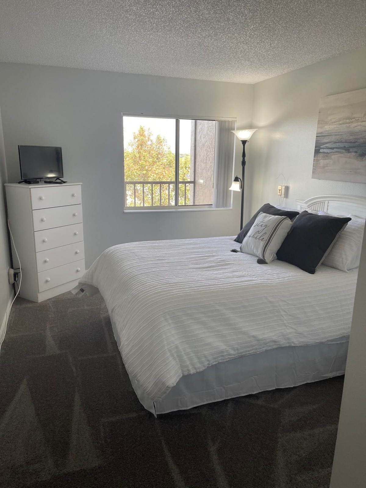 A cozy bedroom with a large bed, white dresser, and a window letting in natural light.