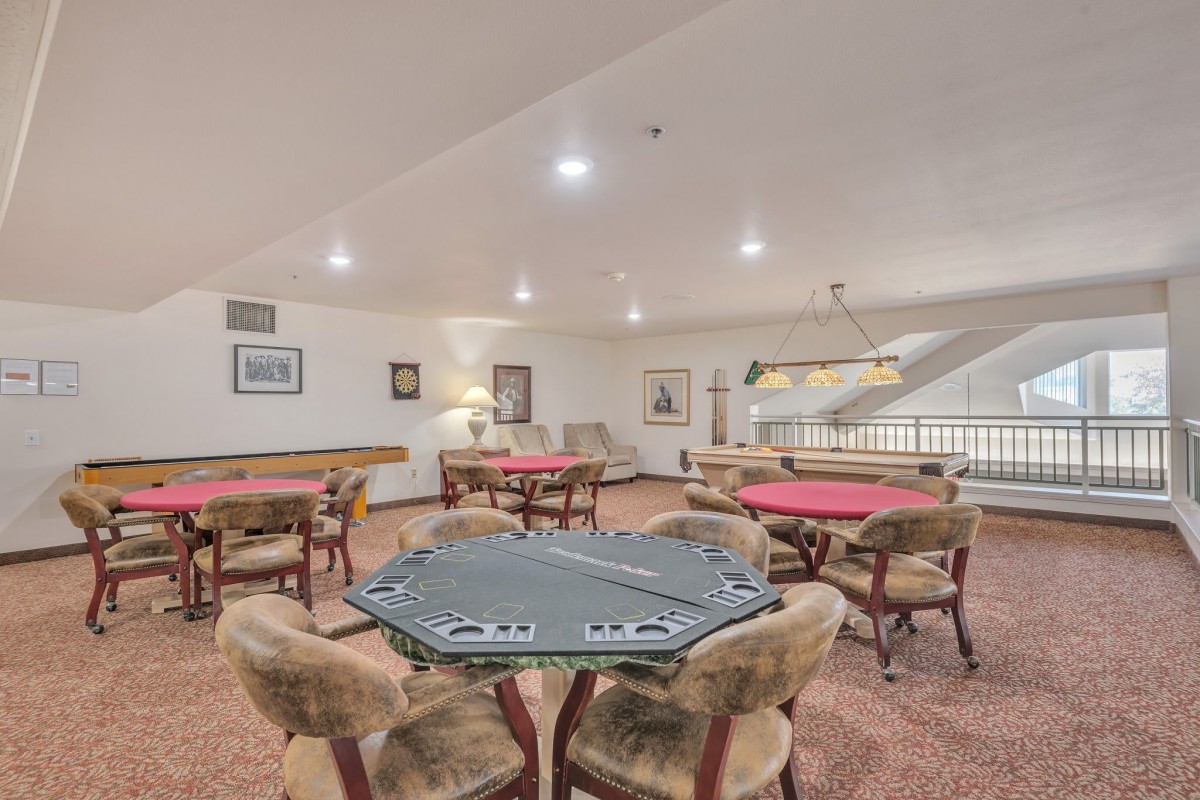 A spacious game room featuring multiple poker tables and comfortable seating under bright lighting.
