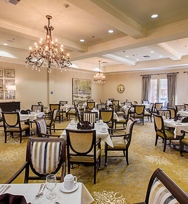 An elegant dining area with neatly arranged tables and chairs, accented by chandeliers.
