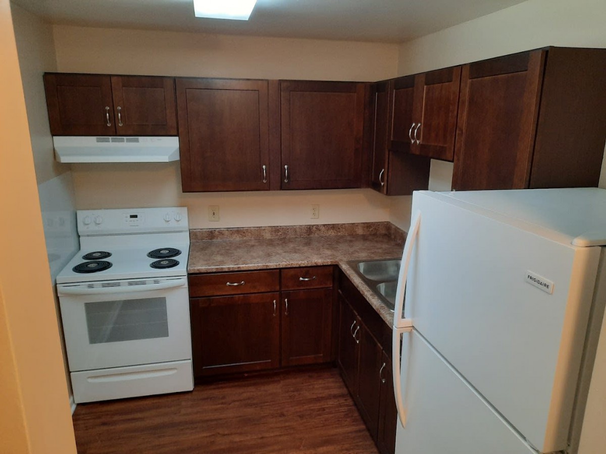 A kitchen with dark wooden cabinets, a white stove and refrigerator, and a tiled countertop.