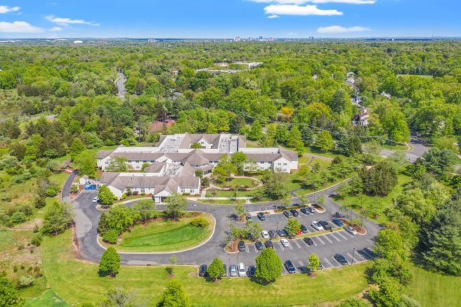 Aerial view of a building surrounded by lush greenery and a parking lot.