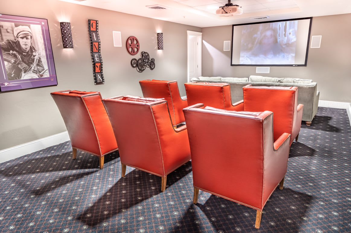 A cozy home theater setup with red chairs arranged in rows facing a large screen.