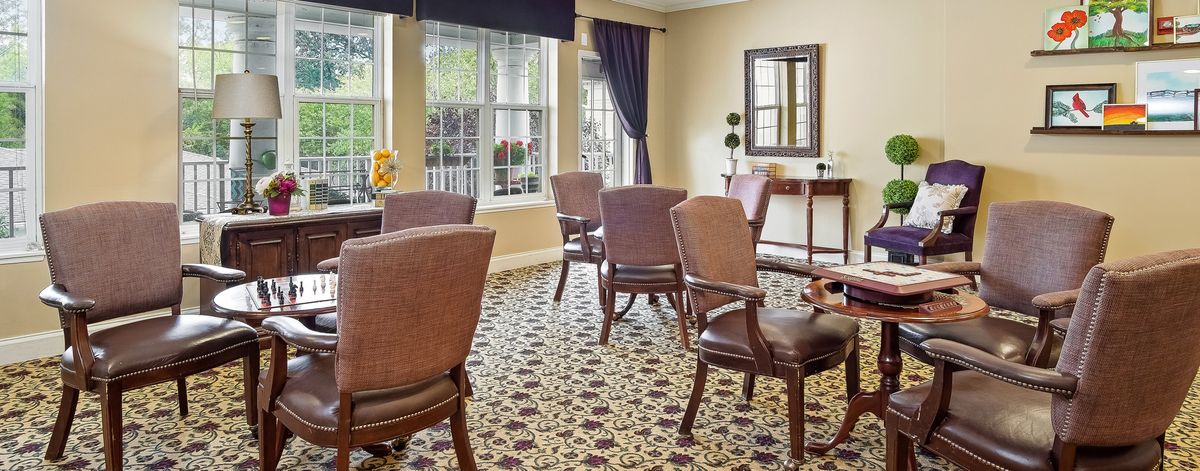 A cozy room with upholstered chairs, patterned carpet, and large windows adorned with drapes.