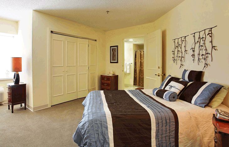 A well-decorated bedroom featuring a bed with striped bedding and decorative pillows, a closet with sliding doors, and wall art.