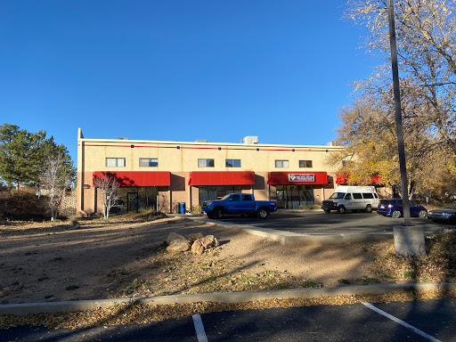 A commercial building with red awnings and parked vehicles against a clear blue sky.