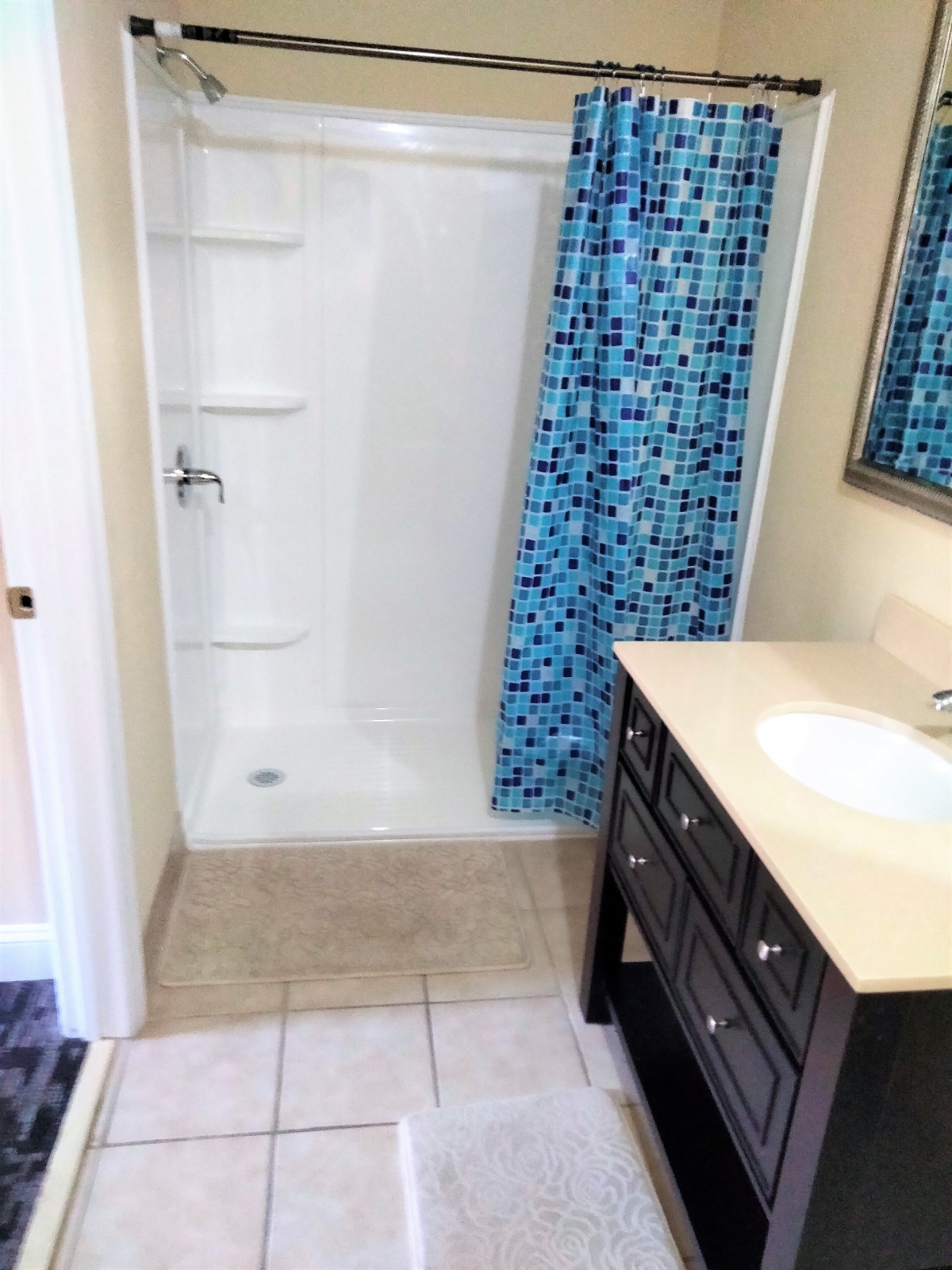 A modern bathroom featuring a shower with blue tile accents and a vanity sink.
